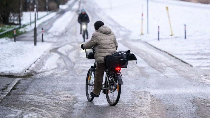  Eine Frau "schlittert" am Morgen mit ihrem Fahrrad über eine schneebedeckte glatte Straße