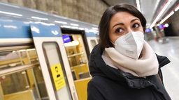 Junge Frau mit FFP2-Mundschutz steht vor einem Waggon