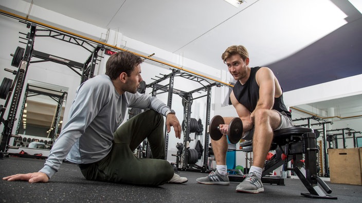 Symbolbild: Ein Mann trainiert vor einem Trainer im Fitnessstudio.