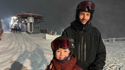 Das Vater-Sohn-Duo Lars und Joel Lockstädt stehen lächelnd auf der flutlichtbeleuteten Skipiste 