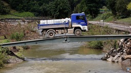 Ein blauer THW-Laster fährt mit Wasserkanistern über eine Behelfsbrücke im Ahrtal.
