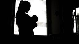 Eine Frau steht mit Baby im Arm in einem dunklen Raum 