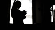 Eine Frau steht mit Baby im Arm in einem dunklen Raum 