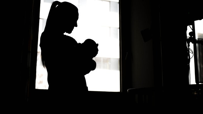 Eine Frau steht mit Baby im Arm in einem dunklen Raum 