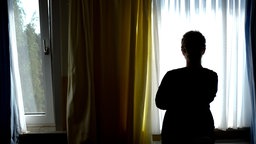 Symbolisch: Eine Frau steht am Fenster eines Frauenhauses und schaut nach draussen
