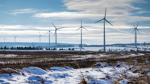 Ein Feld mit Schnee. Im Hintergrund einige Windkrafträder.