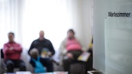 Eine milchige Glastür mit der Aufschrift "Wartezimmer" gibt den Blick auf drei verschwommene Patienten