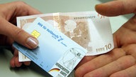 Neue Gesundheitsreform: Eine Hand reicht einen Geldschein und eine Gesundheitskarte einer anderen Hand