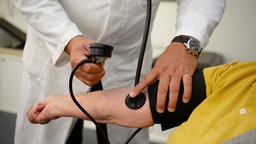 Ein Hausarzt misst in seiner Praxis einer Patientin den Blutdruck.