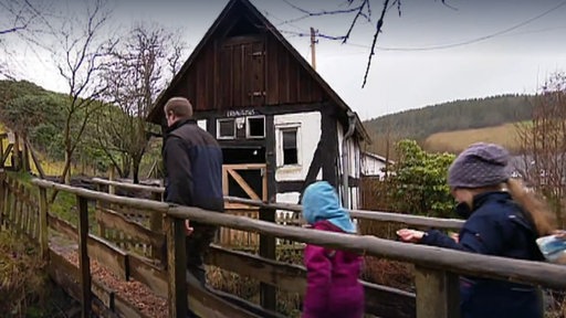 Ein Mann und zwei Mädchen laufen auf ein Fachwerkhaus zu