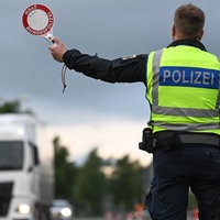 Ein Polizist mit gelber Warnweste hält auf einer Straße einen LKW an