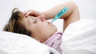 Eine Frau liegt mit einem Fieber-Thermometer im Bett.