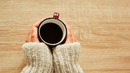 Hände wärmen sich auf an einer Tasse Kaffee