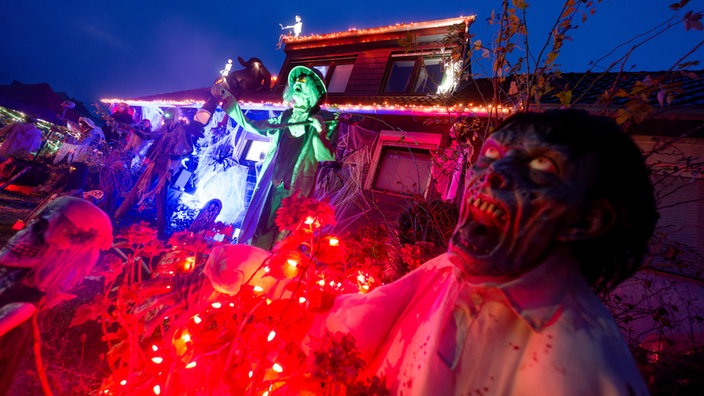 Gruselige Figuren stehen vor dem erleuchteten Halloween-Haus