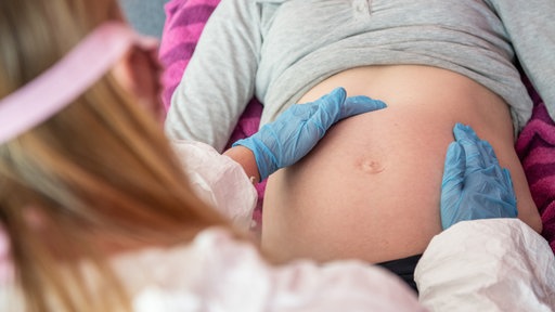 Hebamme untersucht eine schwangere Frau mit Handschuhen