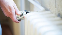 Eine Hand dreht an einem Heizthermostat