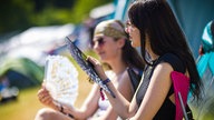 Zwei Frauen sitzen mit Fächern in der Hand in der Sonne 