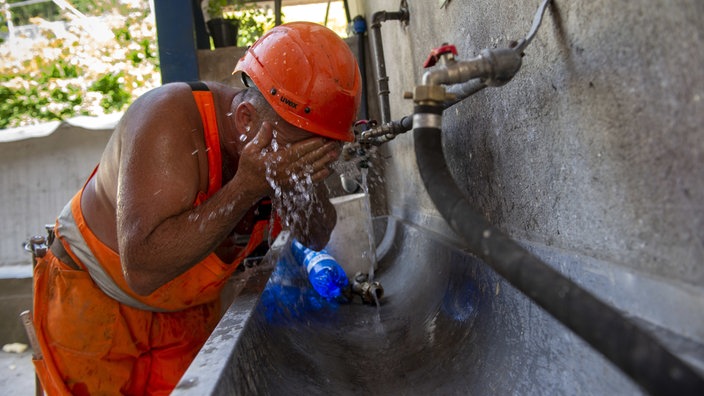 Ein Bauarbeiter einer Strassenbaustelle kühlt sich an einem Wasserhahn ab.