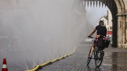Eine Radfahrerin fährt an einer Wassersprühanlage vorbei