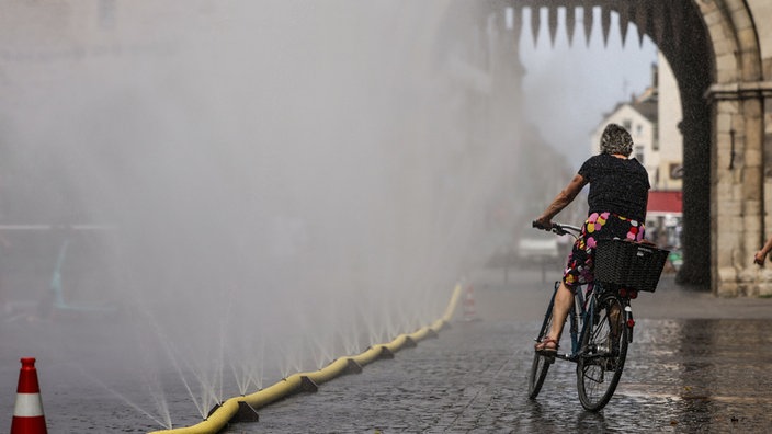 Eine Radfahrerin fährt an einer Wassersprühanlage vorbei