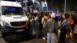 Personen mit Gepäck stehen vor einem Bus und Polizeiauto