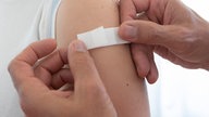 Zwei Hände kleben ein Impfpflaster an einen Arm - Nahaufnahme.