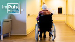 Im Gang eines Pflegeheims sitzt eine alte Frau im Rollstuhl