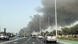Straße mit Autos und einer Rauchwolke im Hintergrund 
