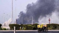 Straße mit Autos und einer Rauchwolke im Hintergrund 