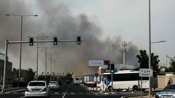 Straße mit Autos und einer Rauchwolke im Hintergrund 
