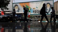 Teheran am Dienstagmorgen: Menschen laufen vor einem Plakat mit Ayatollah Ali Khamenei (links)