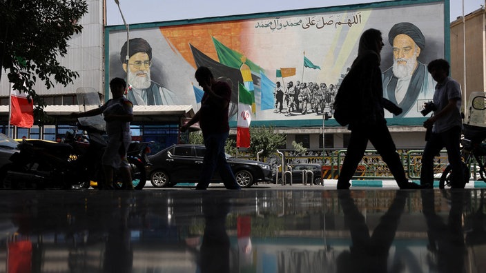 Teheran am Dienstagmorgen: Menschen laufen vor einem Plakat mit Ayatollah Ali Khamenei (links)