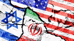 Fotomontage der Flaggen von Israel, Iran und den USA auf gebrochenem Boden
