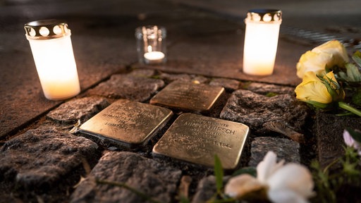 Anlässlich des Jahrestages der nationalsozialistischen und antisemitischen Progrome am 9. November 1938 liegen Blumen und Kerzen auf Stolpersteinen auf der Straße.