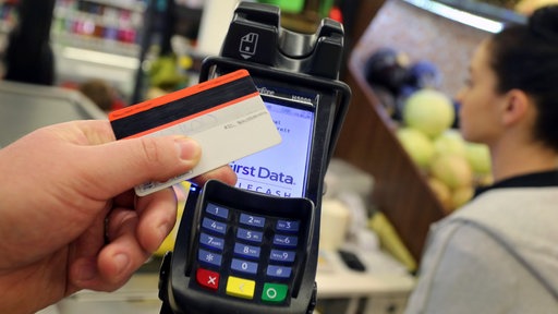 Eine EC-Karte wird an den Bezahl-Terminal an der Kasse eines Supermarktes gehalten.