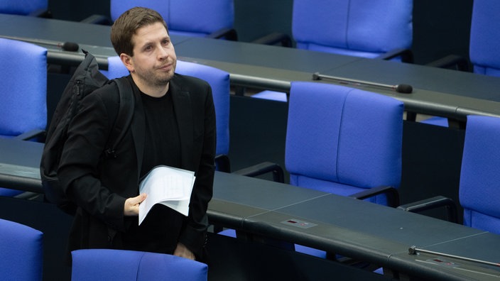 Kevin Kühnert mit geschultertem Rucksack zwischen den blauen Stuhlreihen des Bundestags nach einer Sitzung