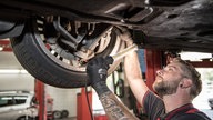 Kfz-Mechatroniker kontrolliert in einer Werkstatt den Unterboden an einem PKW.