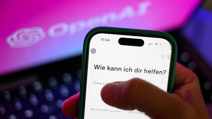 Ein Smartphone mit dem KI-Chatbot ChatGPT ist vor dem Logo des US-Softwareunternehmens OpenAI zu sehen
