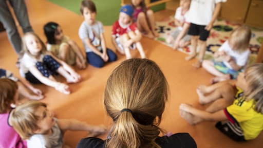 Erzieherin sitzt mit Kindern im Kindergarten im Kreis auf dem Boden
