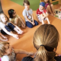 Erzieherin sitzt mit Kindern im Kindergarten im Kreis auf dem Boden