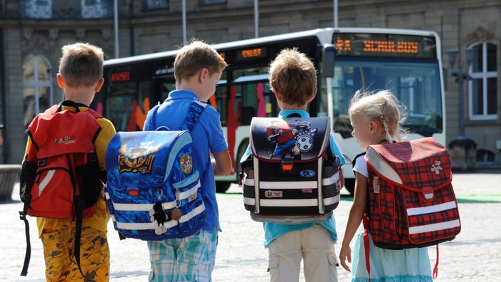 Vier Kinder mit Tonistern auf dem Rücken warten auf den Bus