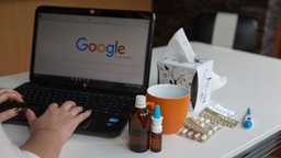 Eine Person schaut ihre Krankheitssymptome im Internet nach, neben ihr steht Medizin