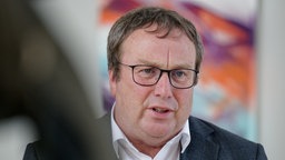 Porträt Oliver Krischer (Grüne), er trägt einen dunklen Anzug und ein weißes Hemd ohne Krawatte