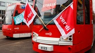 Streikende stehen mit Flaggen vor parkenden Stadtbahnen.