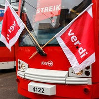 Streikende stehen mit Flaggen vor parkenden Stadtbahnen.