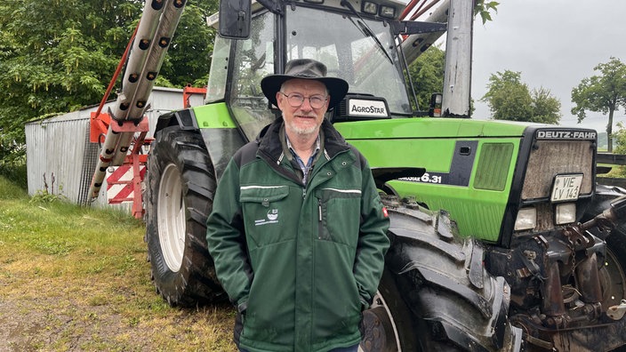 Im Vordergrund steht NRW-Landwirt Paul-Christian Küskens. Hinter ihm sieht man einen Traktor.