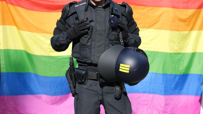 Ein Polizist steht vor einer Regenbogenflagge