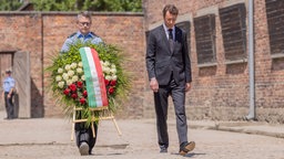 Hendrik Wüst läuft neben einem Beamten der Blumen trägt in Auschwitz