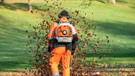 Ein Arbeiter beseitigt Laub in einem Park mit einem Laubbläser