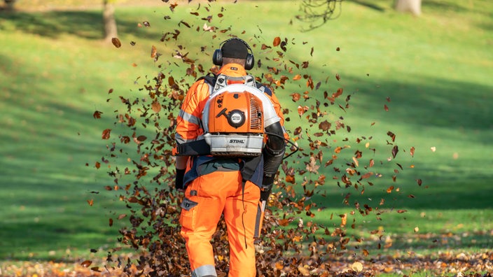 Ein Arbeiter beseitigt Laub in einem Park mit einem Laubbläser
